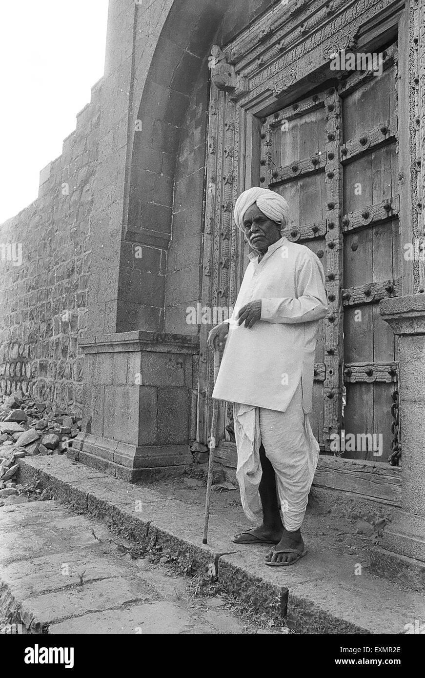 Old man standing in front of massive old ancestral home with intricately carved door Munagoli village Bijapur Karnataka Stock Photo