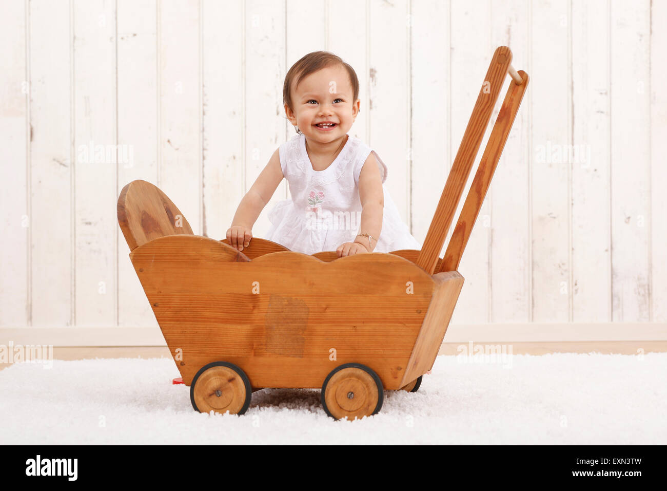 Portrait of smiling baby girl playing with wooden doll buggy Stock