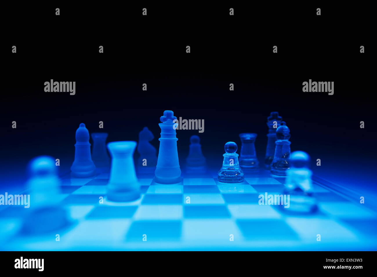 Chess pieces on blue glass board against dark background Stock Photo