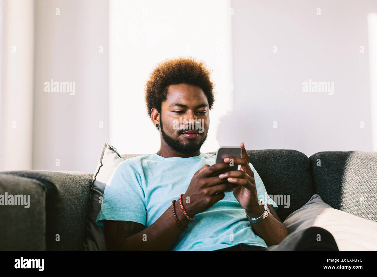 Young man at home reading messages on smart phone Stock Photo