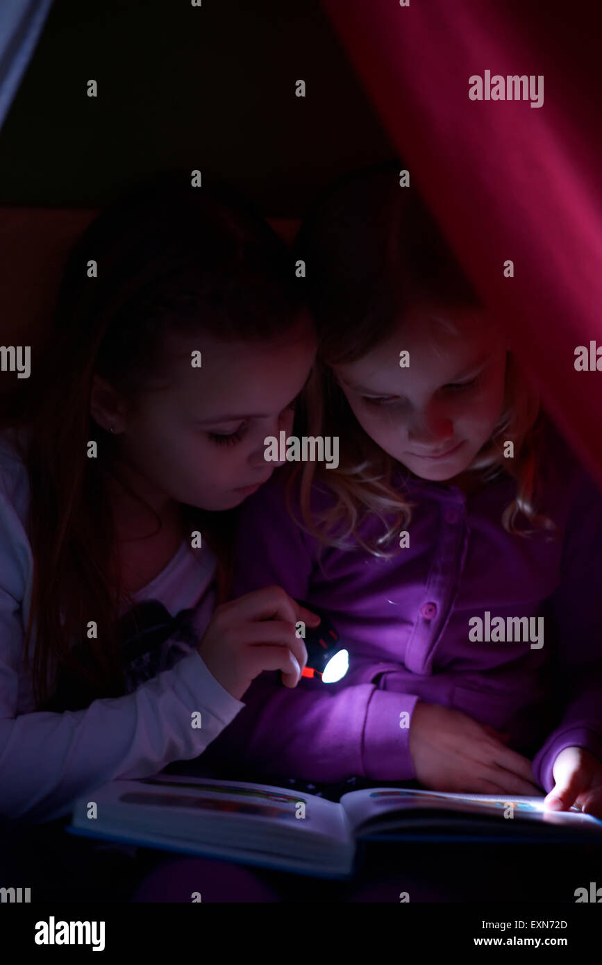 Two girls reading a book with a torch in their selfmade cave Stock Photo