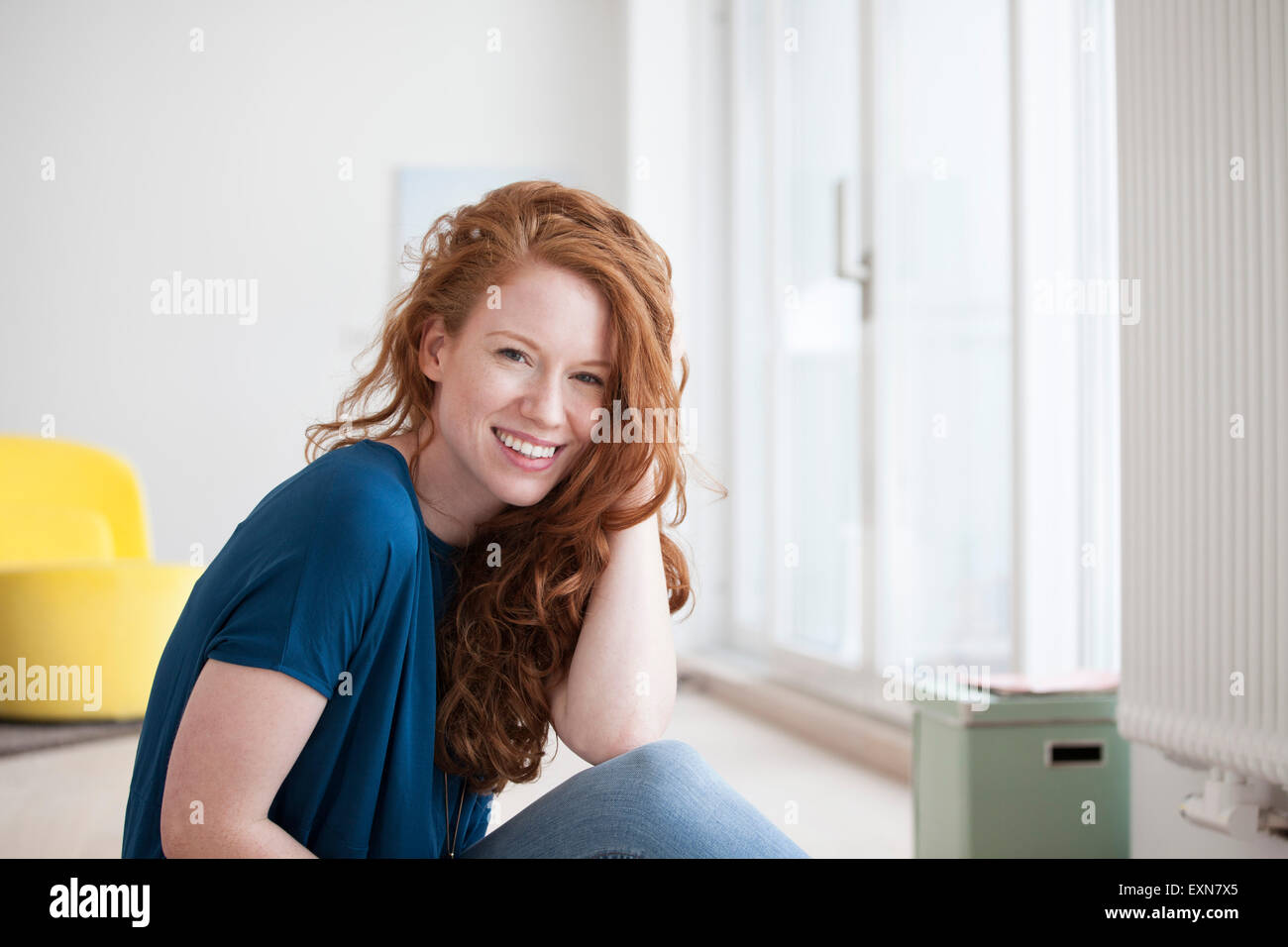 Portrait of happy young woman sitting on the floor of her living room ...