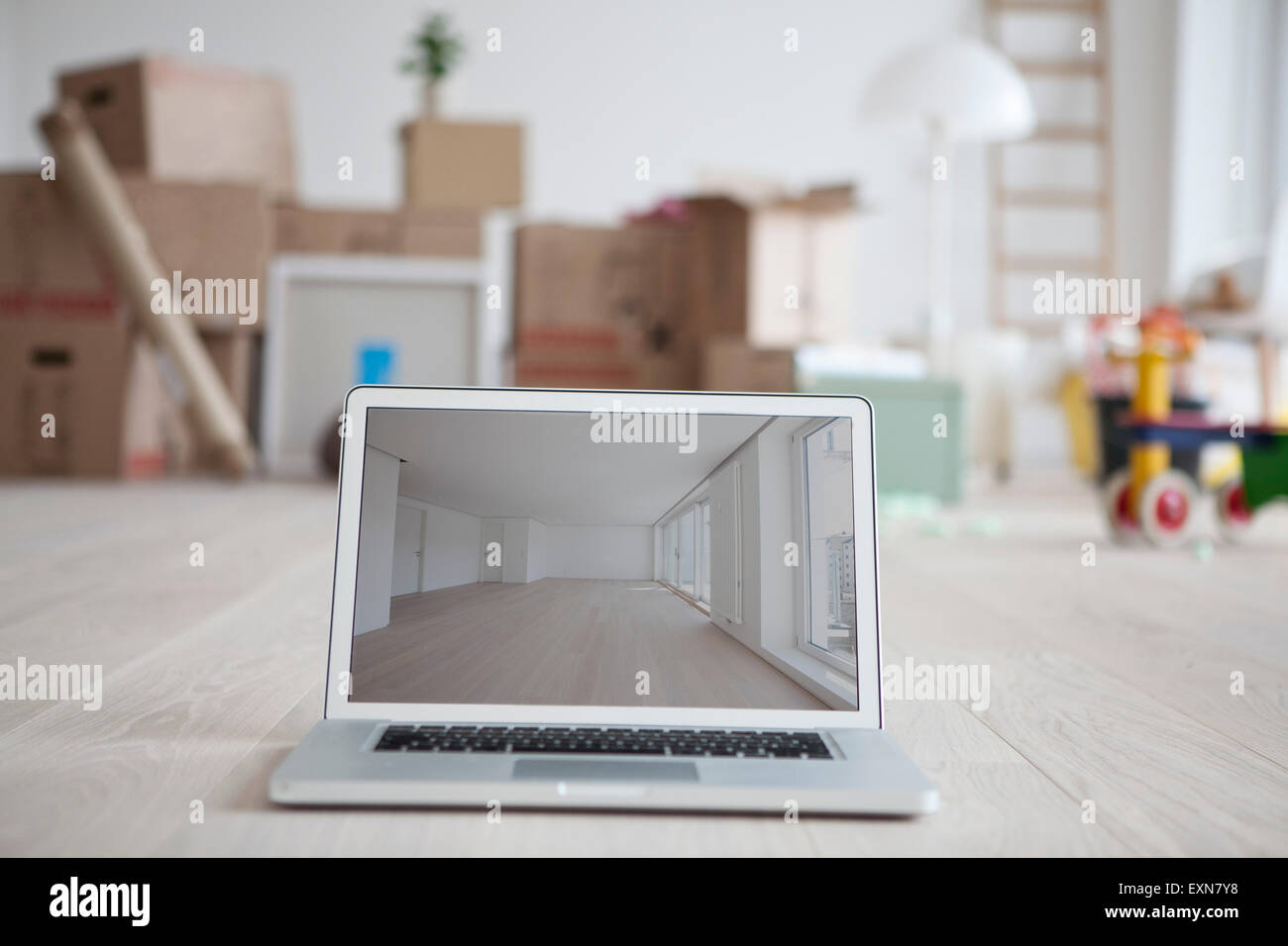 Laptop with picture of empty room in front of piled cardboard boxes Stock Photo
