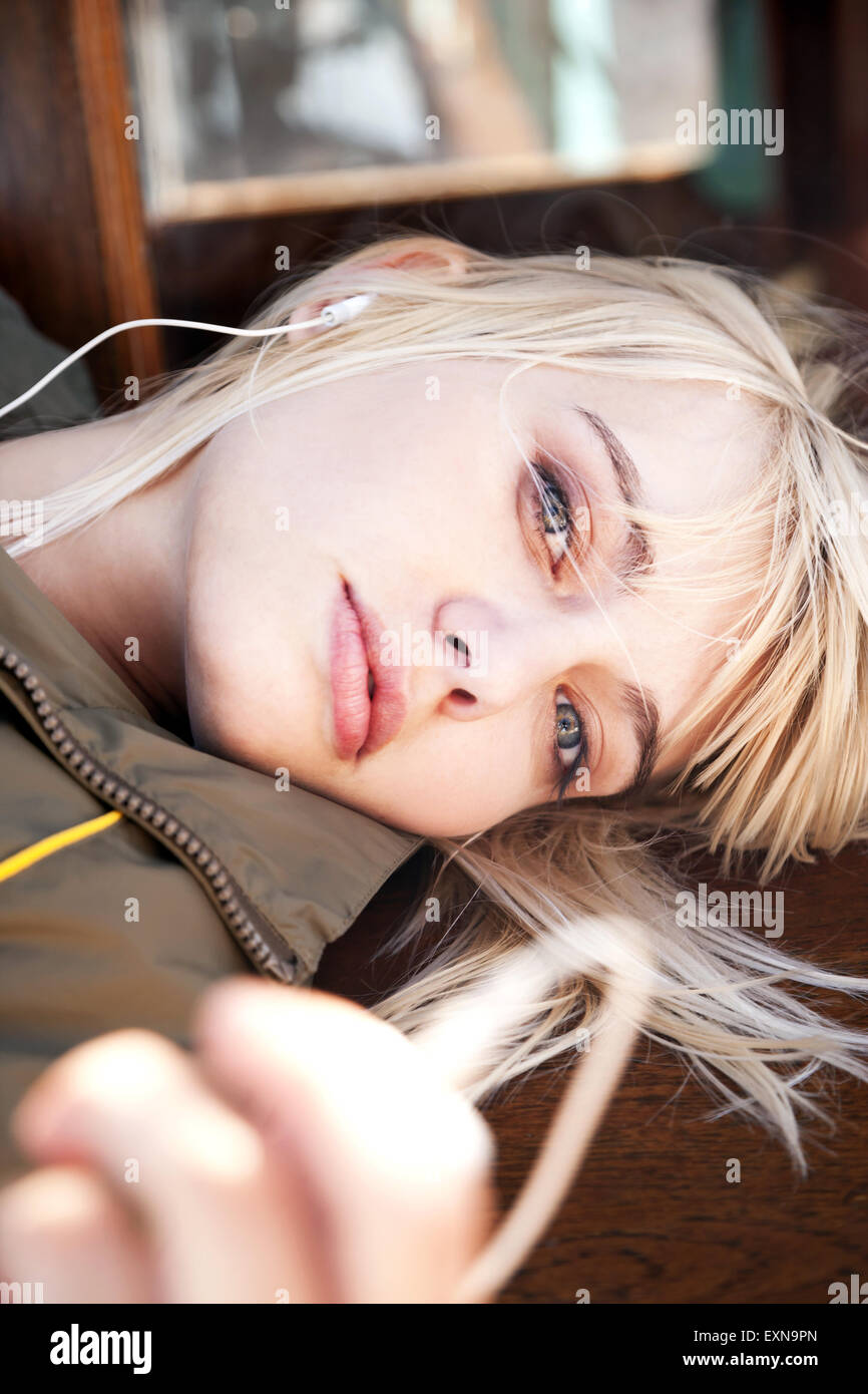 Relaxed young woman lying on a bench listening to music Stock Photo - Alamy