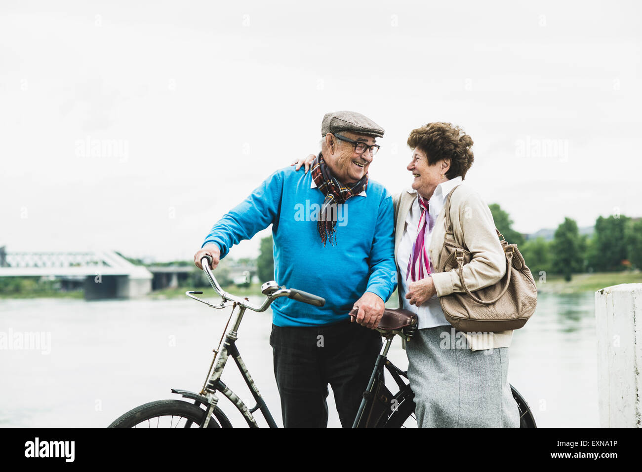 Happy senior couple standing at water's edge with bicycle Stock Photo