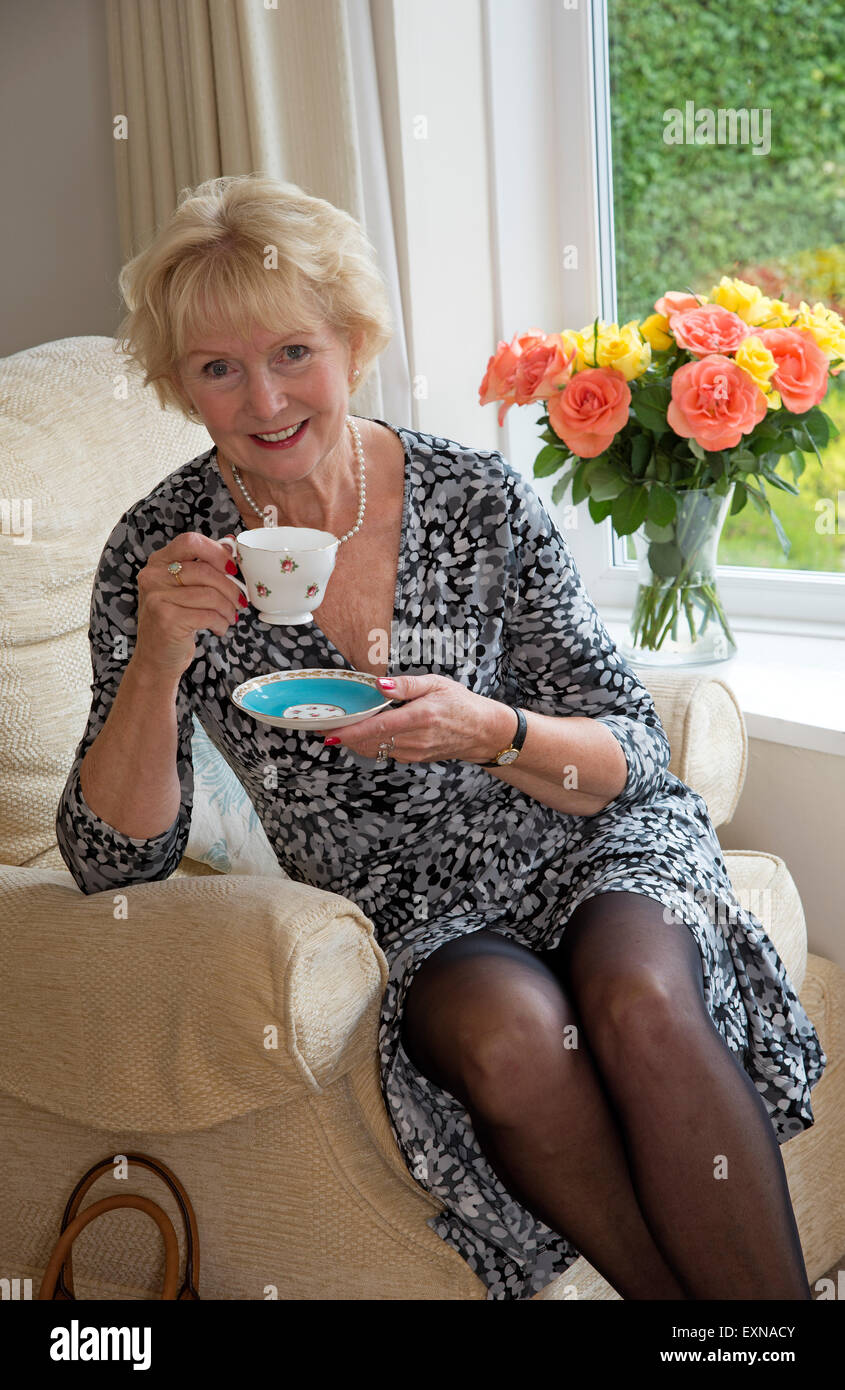 Elderly woman sitting in a comfortable chair having a cup of tea Stock Photo