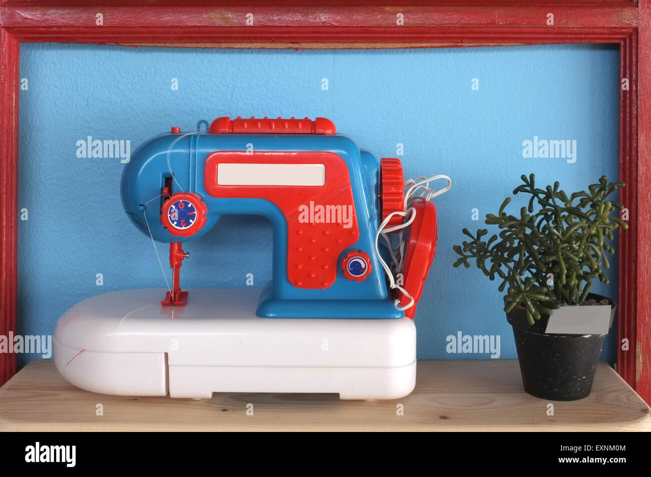 Toy and vintage sewing machine on blue background with pot of plant Stock Photo