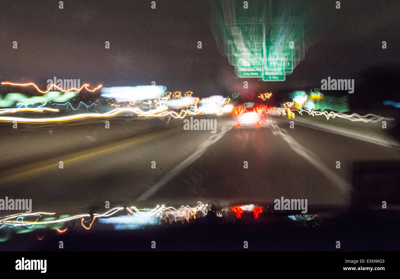 A time-lapsed view of a vehicle driving down a highway at night, with headlights and street lights blurred. Stock Photo