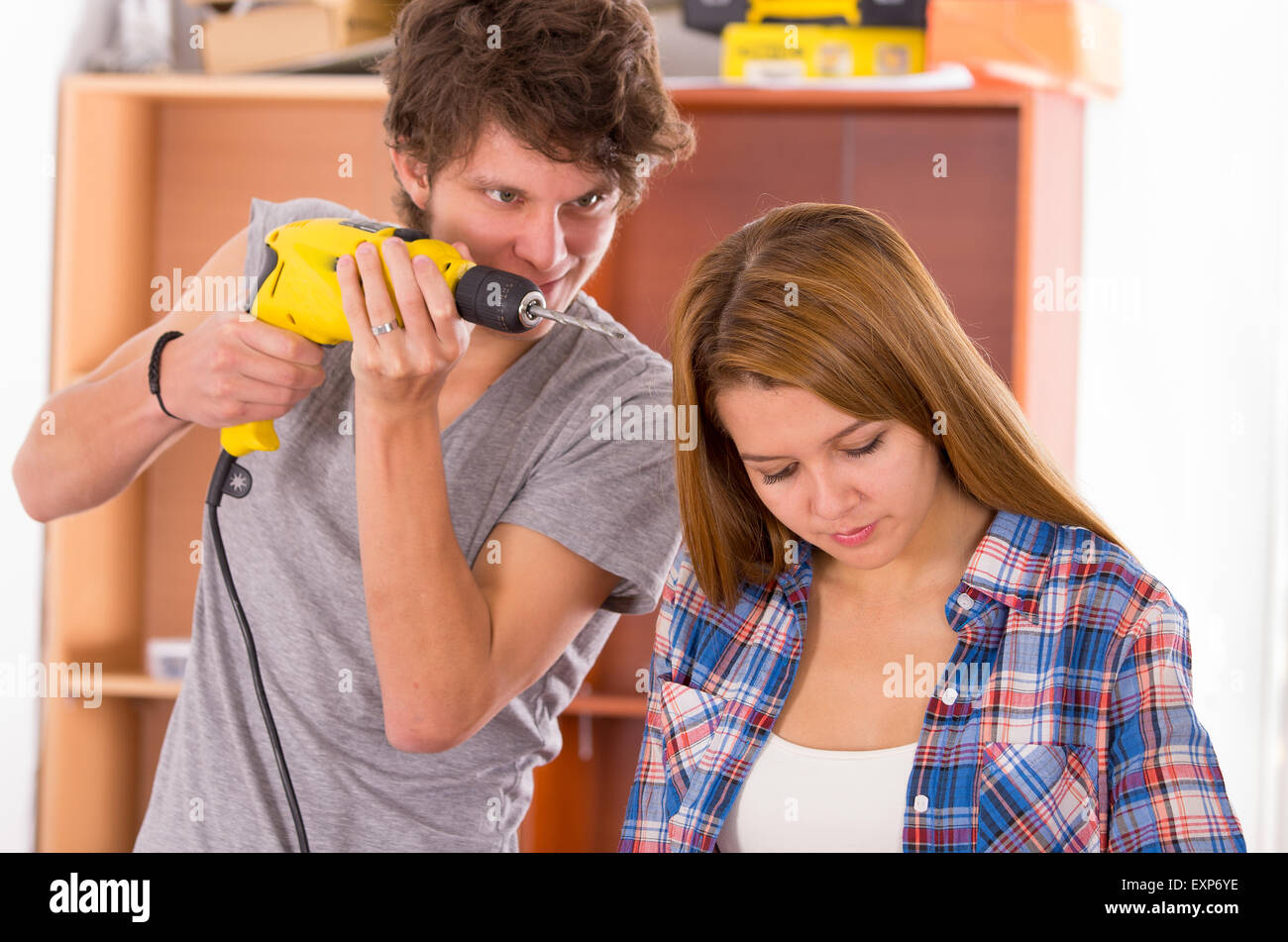 Couple in renovation process standing together with woman looking down and man holding up power drill next to her head Stock Photo