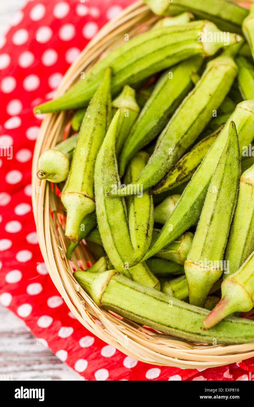 Green okra vegetable on red napkin against white wooden background
