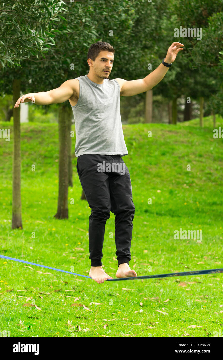 Man walking on slackline in park with arms out maintaining balance and