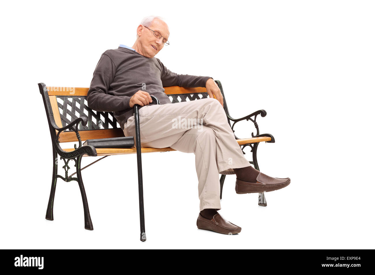 Studio shot of an old man with cane sleeping on a wooden bench with a book beside him isolated on white background Stock Photo