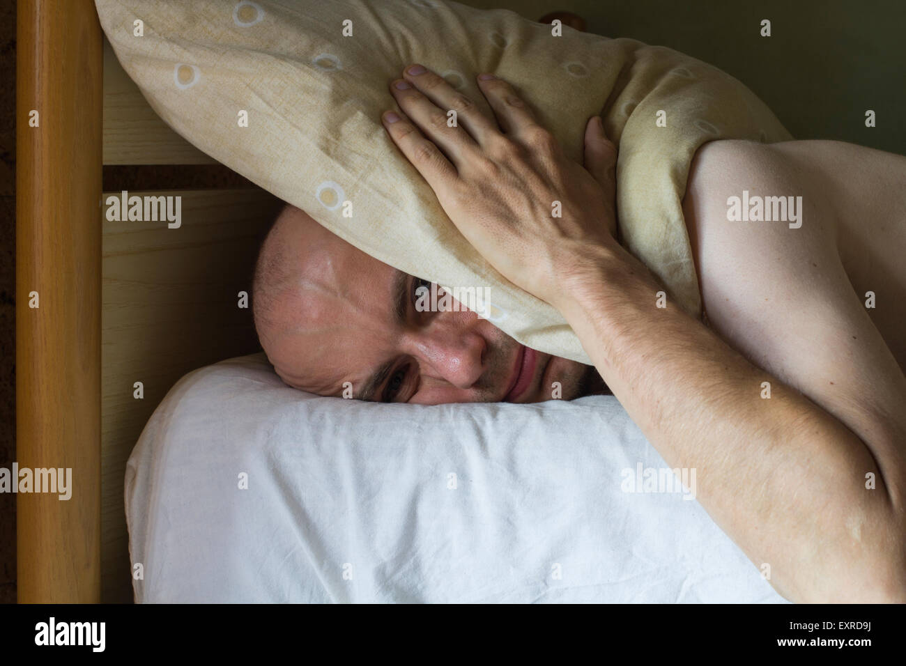 White sad man on the bed with a pillow over his head Stock Photo