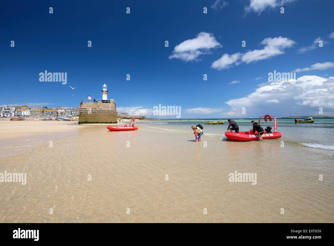 St Ives, Cornwall, UK: Family getting out of a red self-drive hire boat in the shallow water of the harbour beach on sunny day. Stock Photo