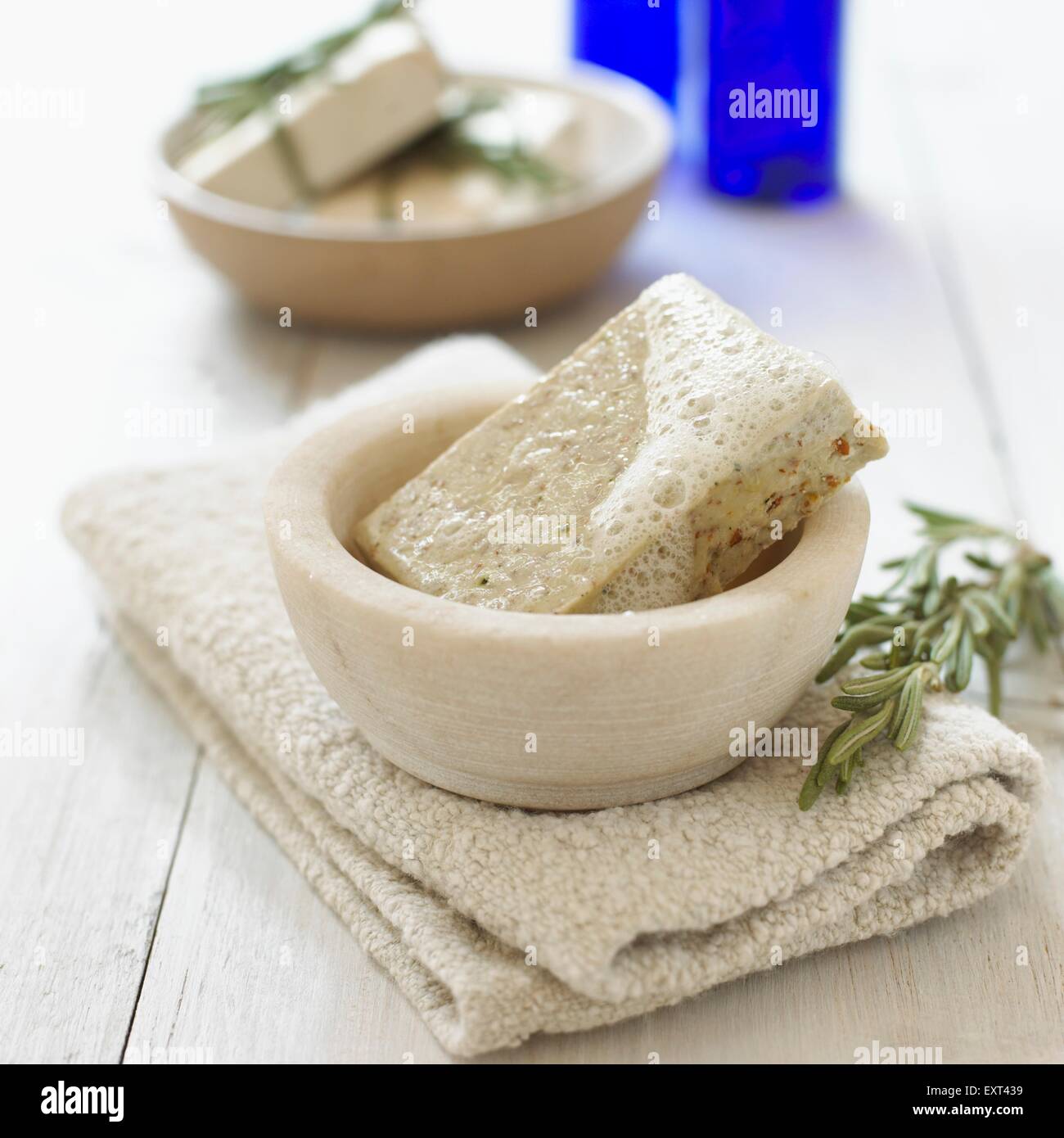 Rosemary soap in a bowl, folded towel underneath and a fresh sprig of rosemary nearby Stock Photo