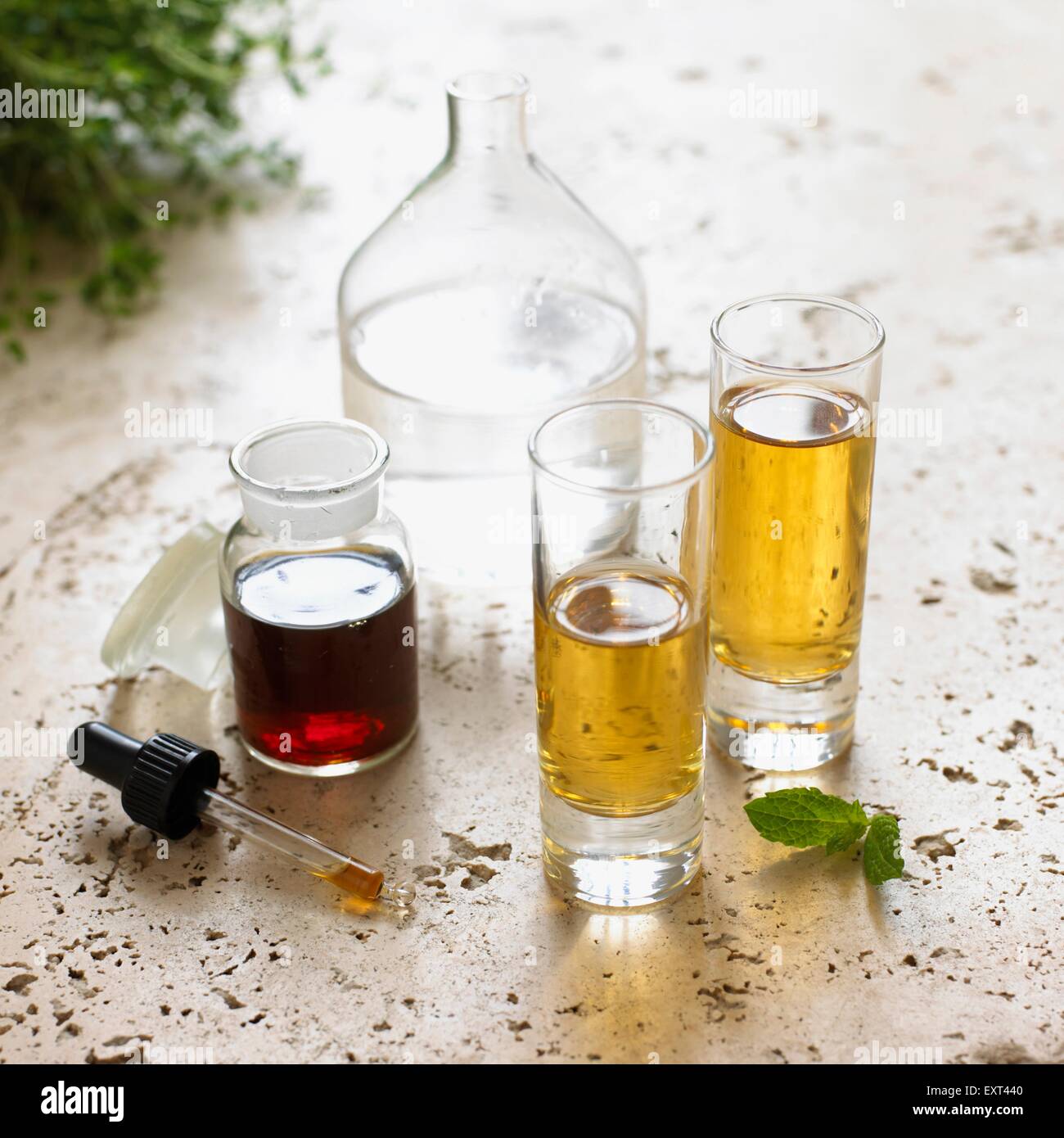 Peppermint and thyme tincture in bottle and pipette, and two glasses containing tincture diluted with water Stock Photo
