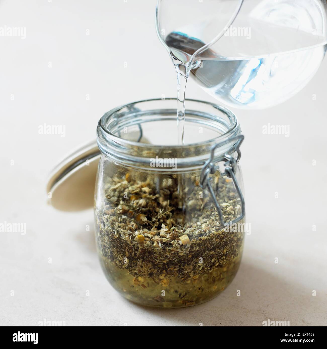 Making herbal tincture, pouring vodka into jar holding peppermint, thyme, chamomile, yarrow, liquorice root Stock Photo