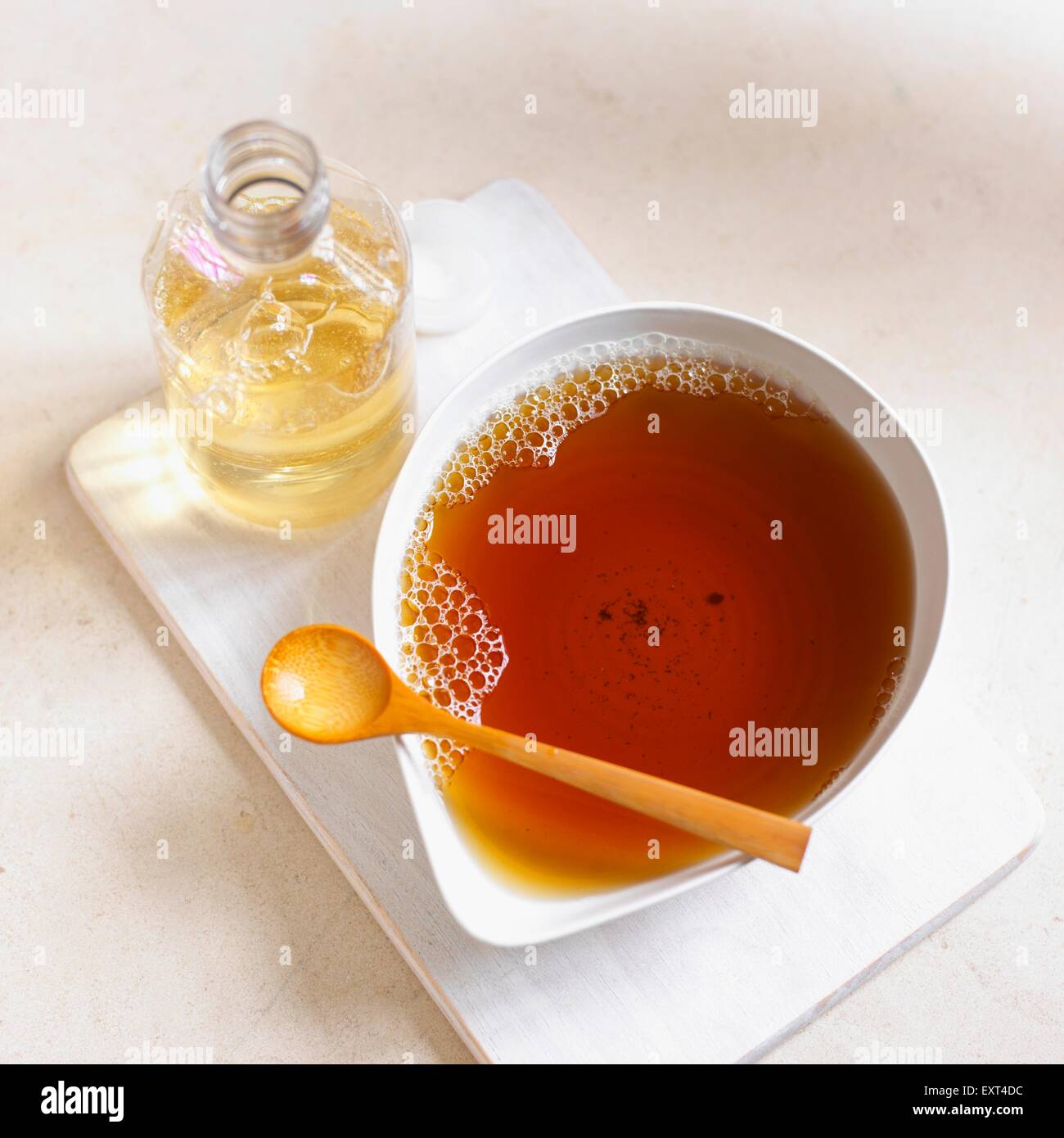 Home made hair tonic in white bowl with wooden spoon and bottle on chopping board Stock Photo