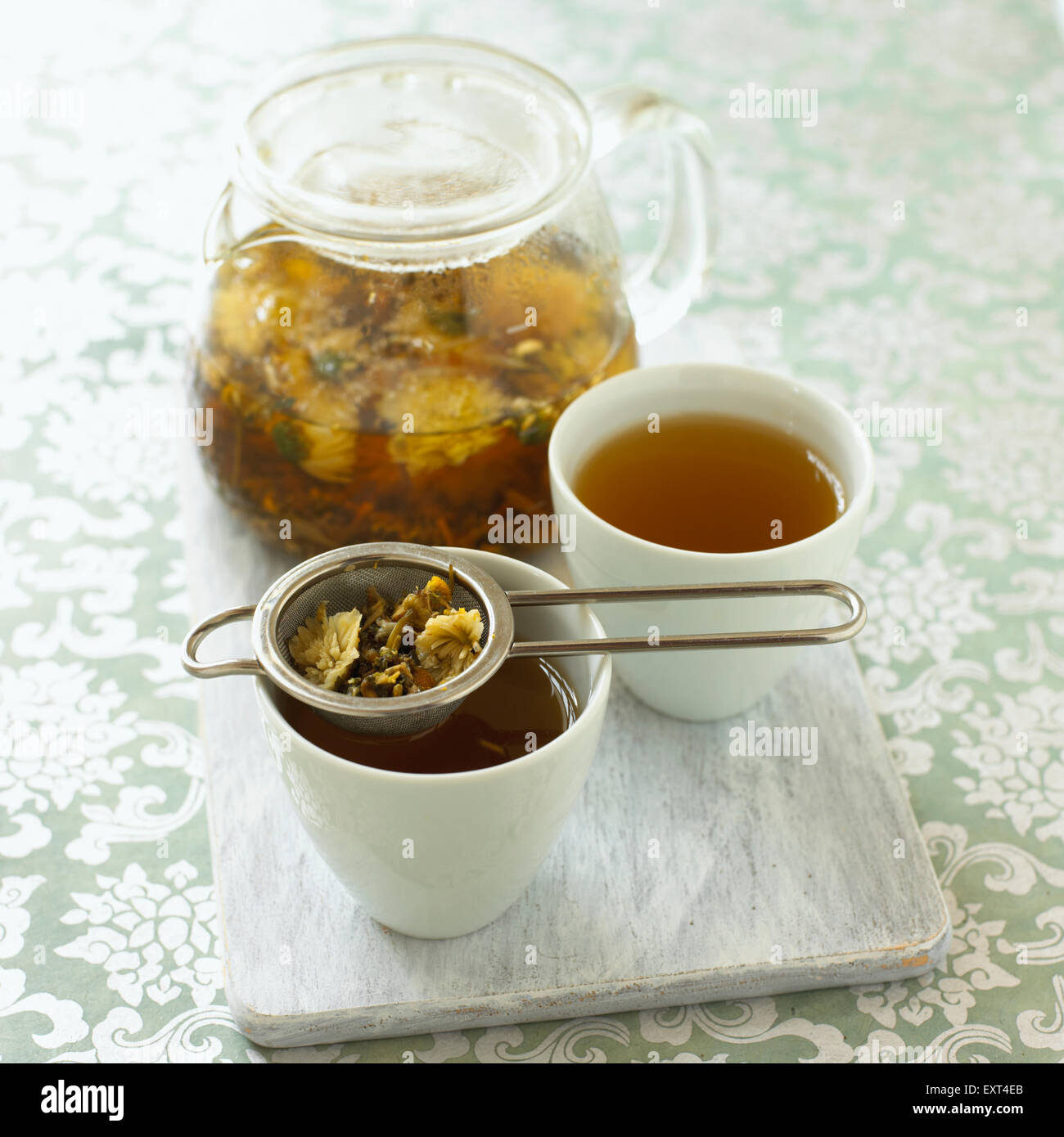 Chamomile tea in teapot and in cup with strainer resting on top Stock Photo