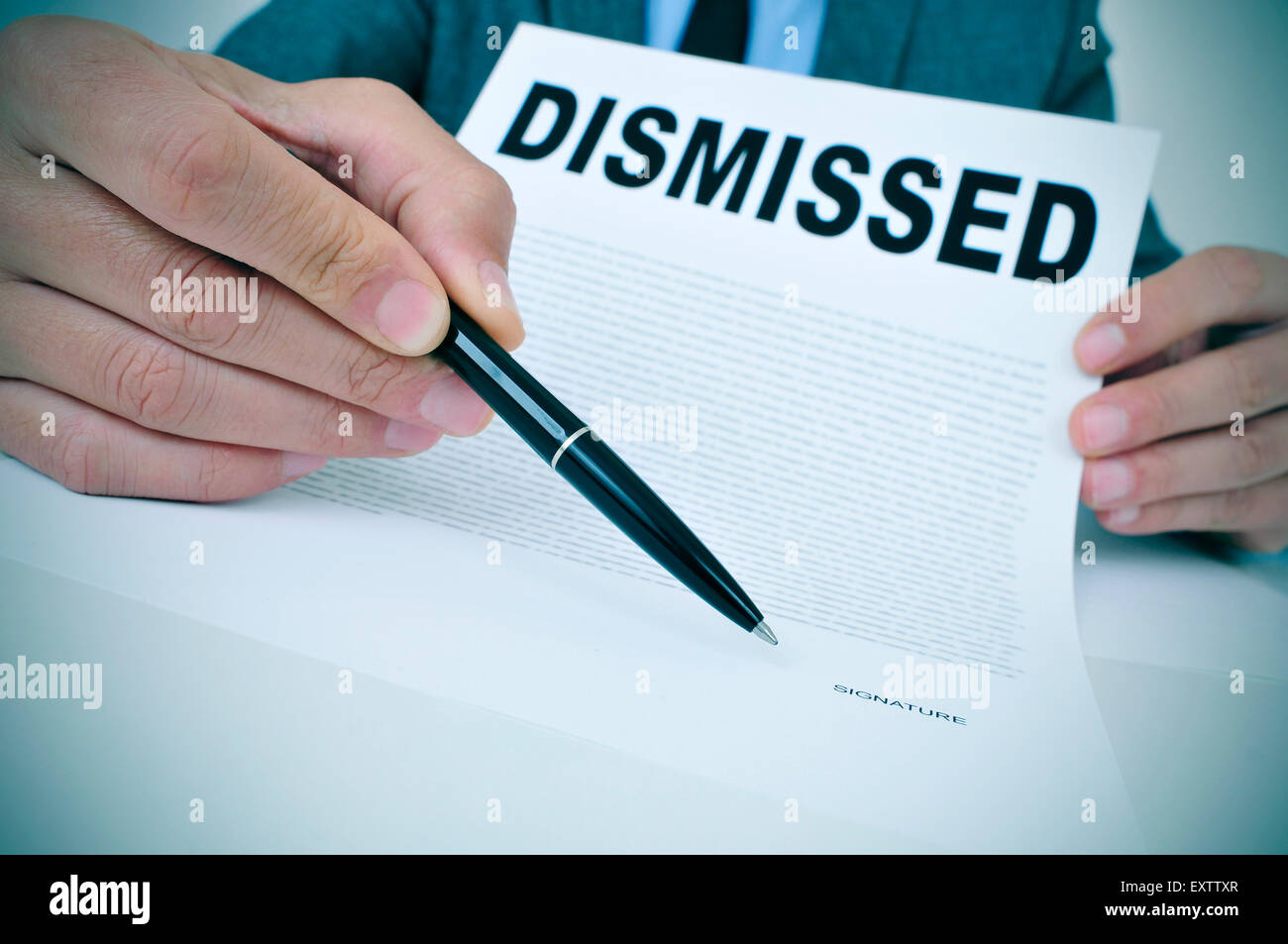 a young businessman sitting at his office desk shows a document with the word dismissed written in it and points with a pen wher Stock Photo