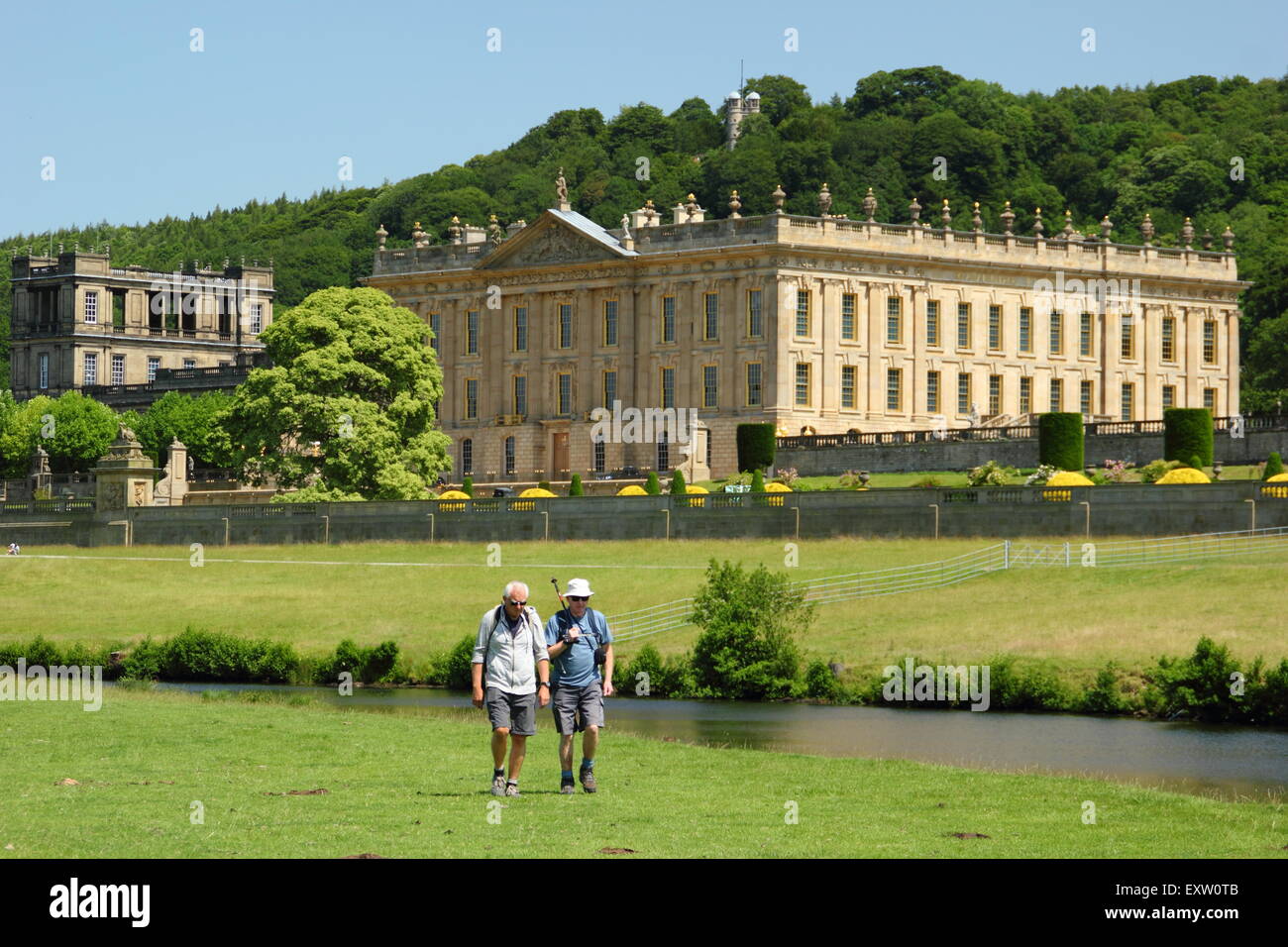 Two men walk on the banks of the River Derwent by Chatsworth House in the Peak District on a glorious summer day, Derbyshire UK Stock Photo