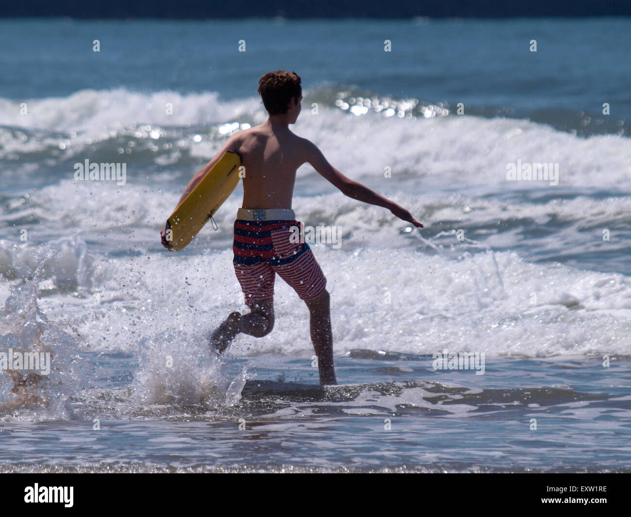 Teenage boy with bodyboard running into the sea, Woolacombe, Devon, UK Stock Photo