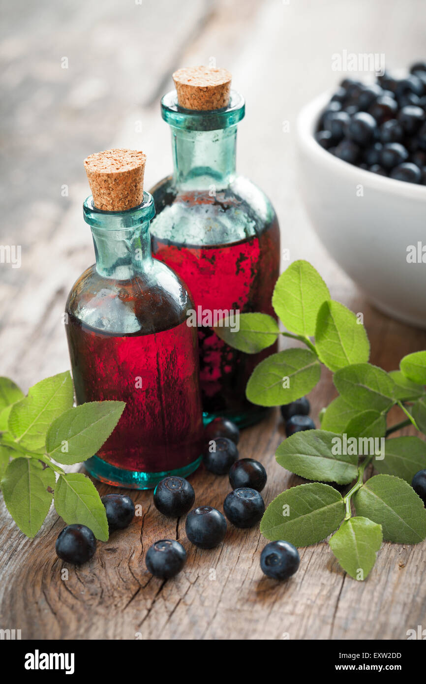 Two vintage bottles of tincture or cosmetic product and bowl with blueberries on wooden table. Stock Photo