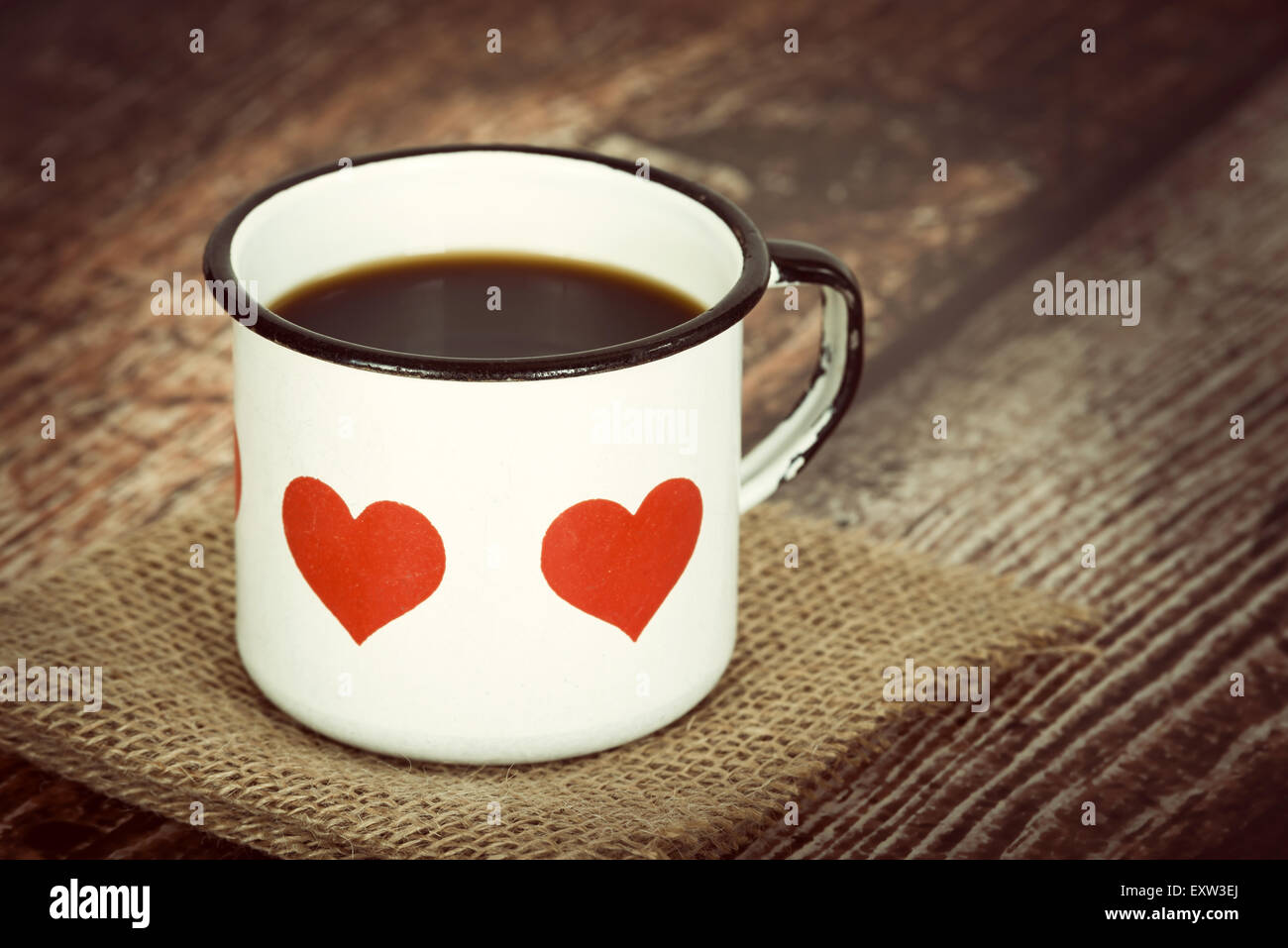 A cup of coffee in an old enamel mug with hearts against vintage background Stock Photo