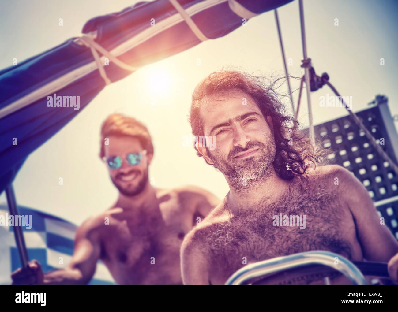 Two men on sailboat, traveling along sea, water trip in the evening in bright sunset light, summertime activity Stock Photo