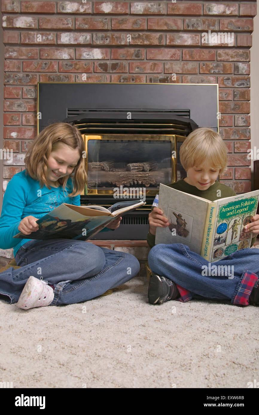 Boy and girl enjoying reading in front of a gas fireplace in a family room. Concepts informal