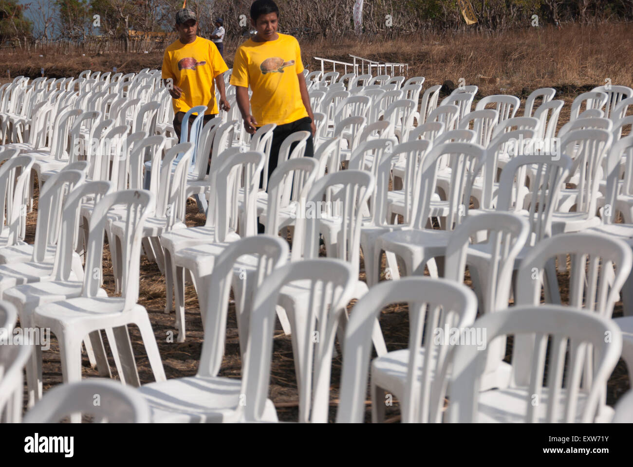 Men wearing snake-necked turtle shirts walking on aisle between rows of white plastic chairs. Stock Photo