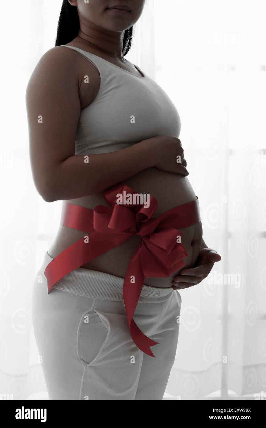 Pregnant woman standing with red ribbon on the abdomen, Stock Photo