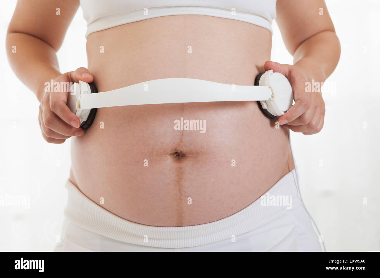 Pregnant woman holding head phones on the abdomen, Stock Photo