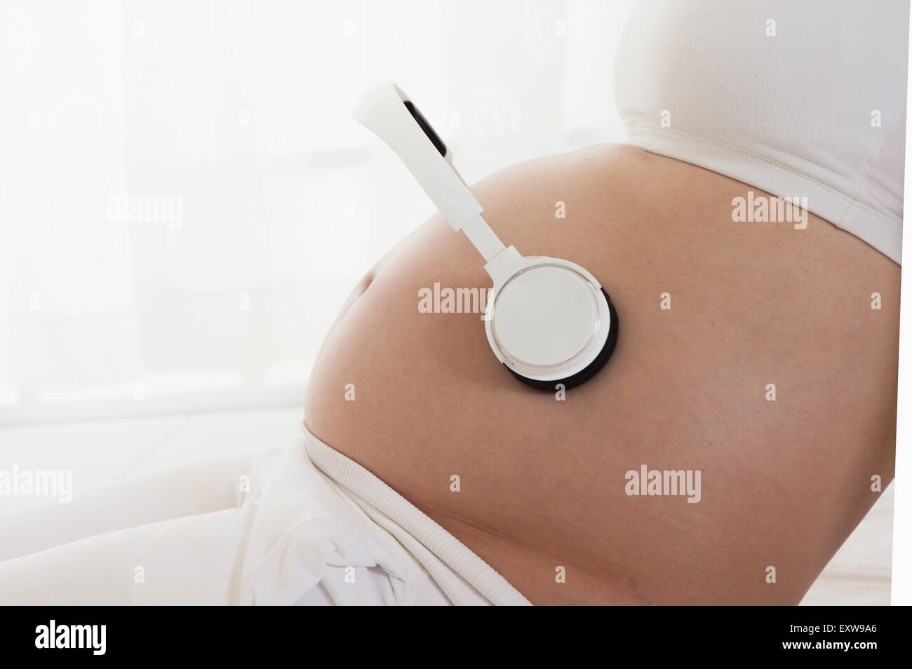 Pregnant woman holding head phones on the abdomen, Stock Photo