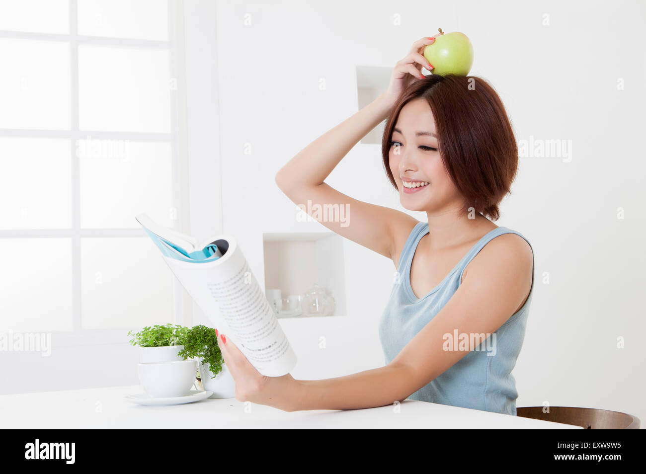 Young woman holding an apple and reading a book with smile, Stock Photo