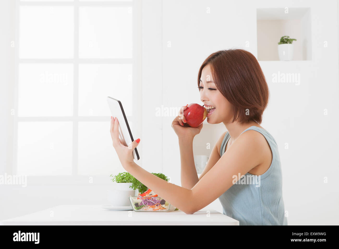 Young woman holding an apple and using touch pad, Stock Photo