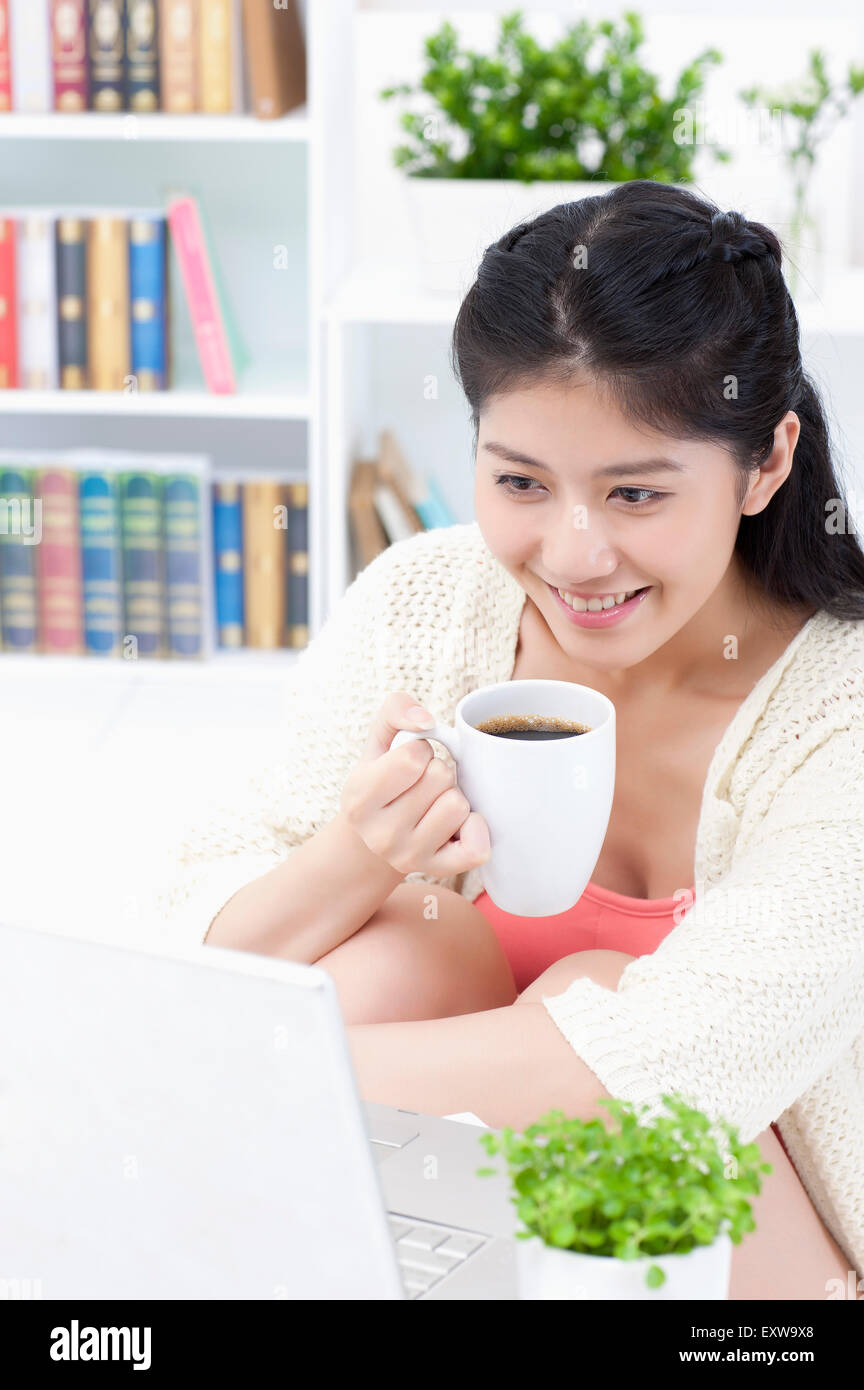 Young woman holding a cup of coffee and looking at the laptop, Stock Photo