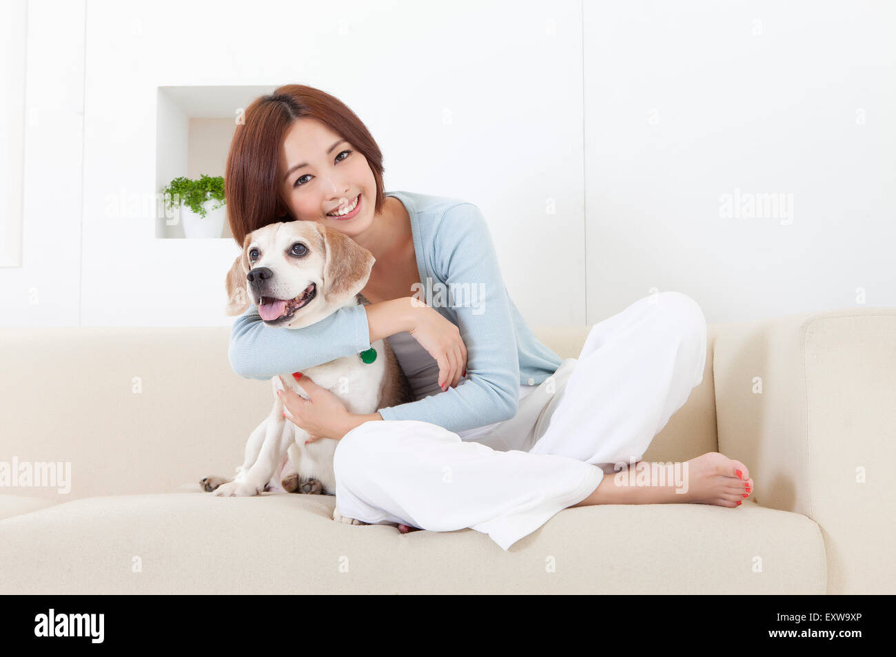 Young woman sitting on the sofa with her dog and smiling at the camera, Stock Photo