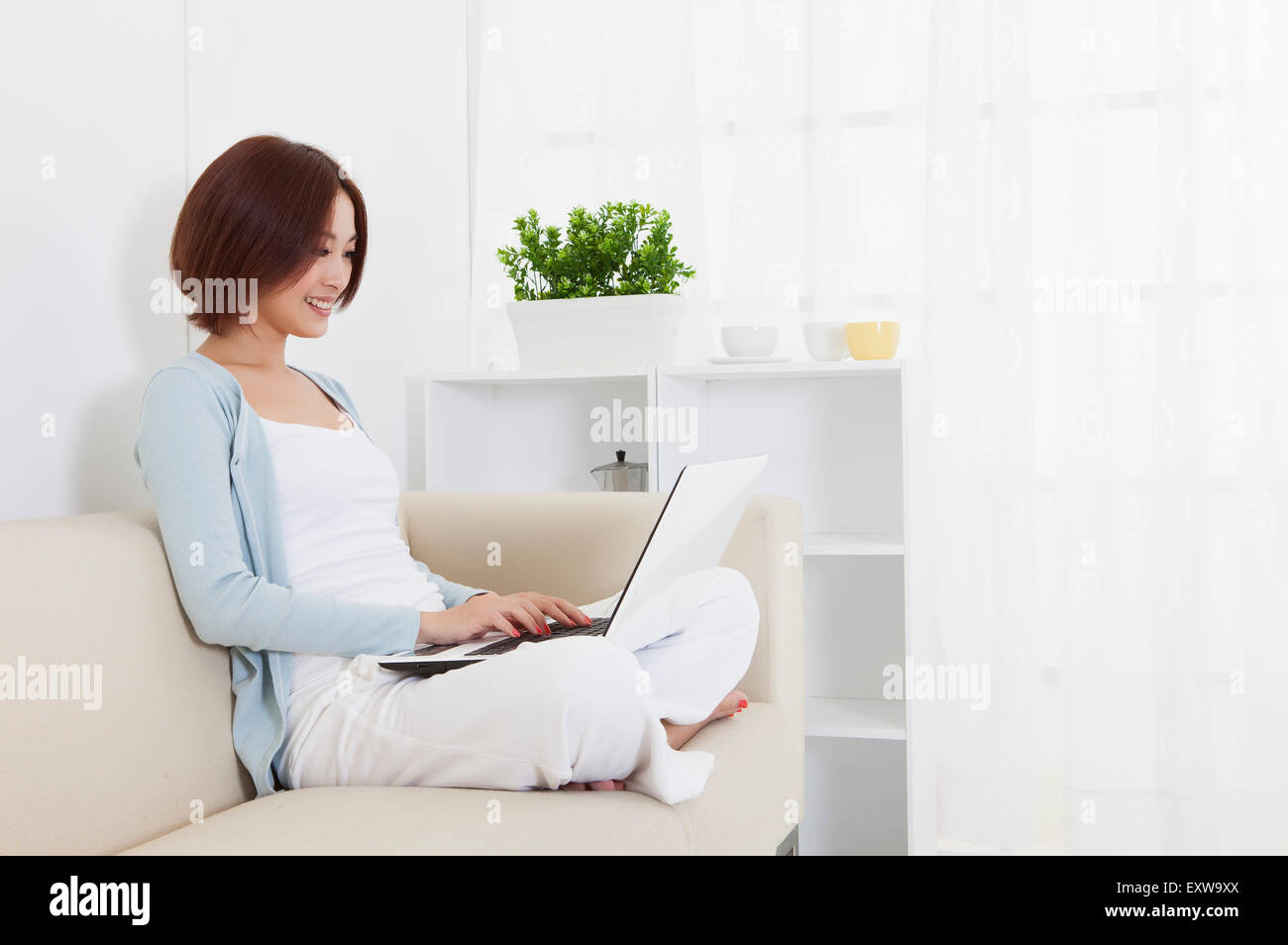 Young woman sitting on sofa and using laptop, Stock Photo