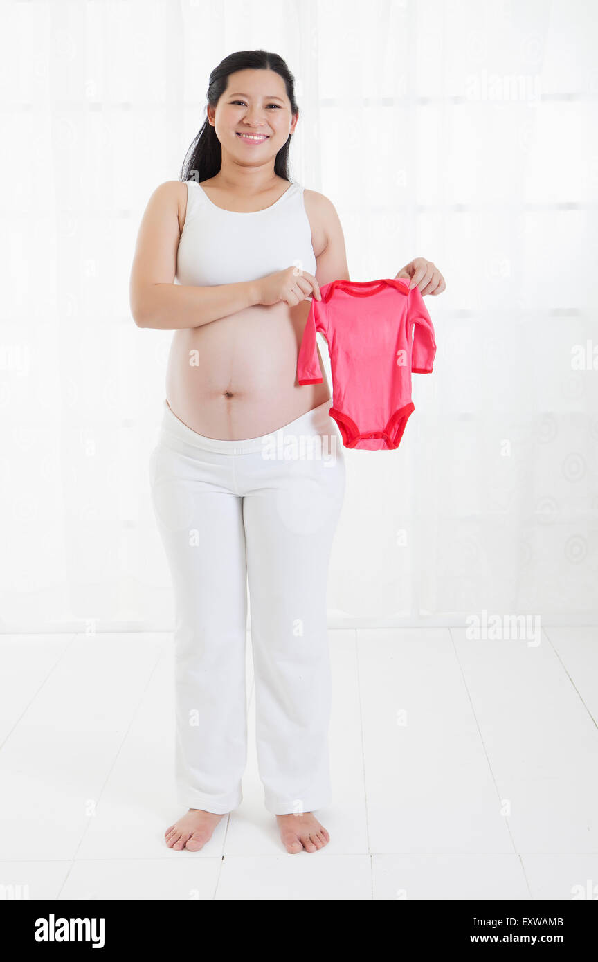 Pregnant woman holding baby clothing and smiling at the camera, Stock Photo