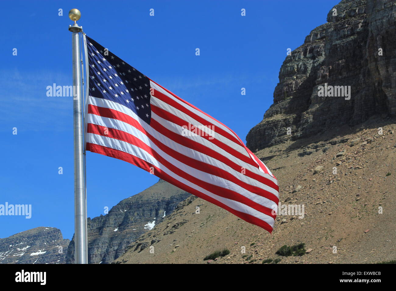 American flag, showing the full stars and stripes, on a silver flagpole blowing in the wind against a blue sky and mountains Stock Photo