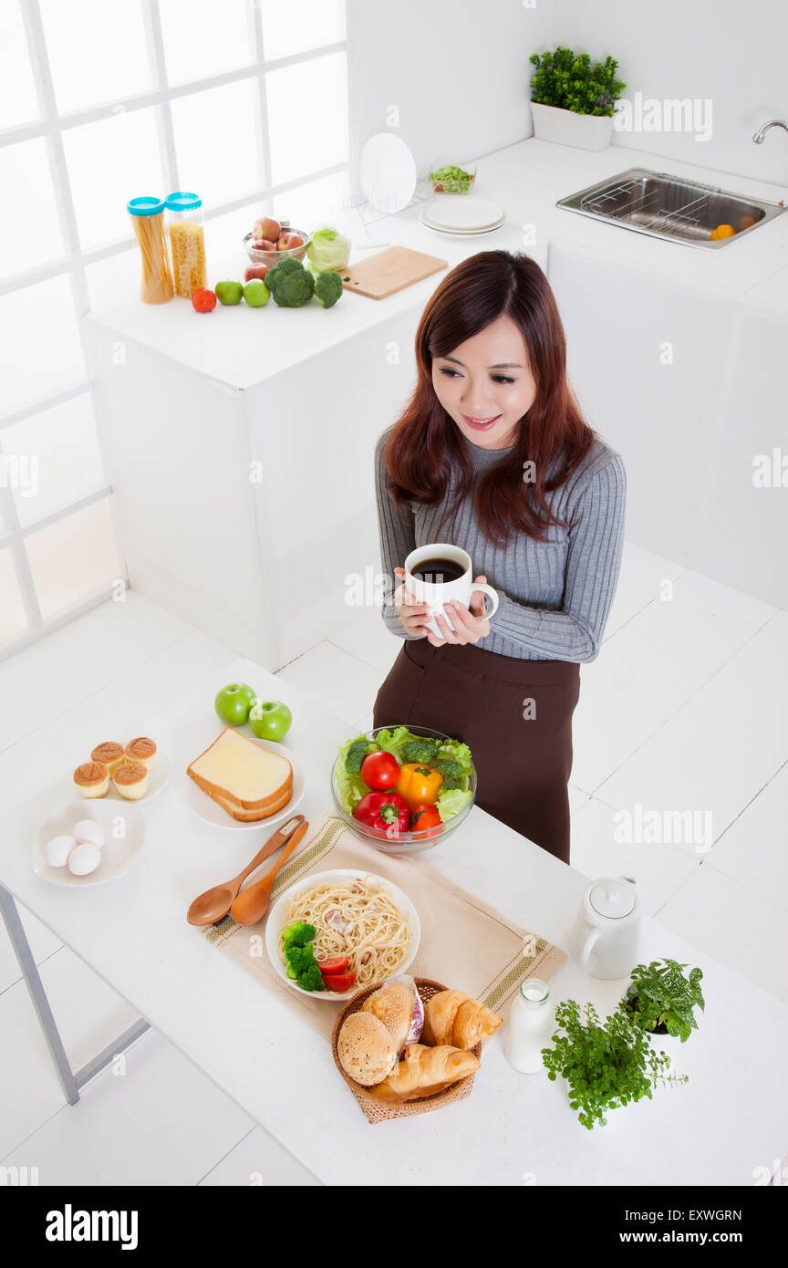 Young woman holding a cup of coffee and standing in the kitchen with smile, Stock Photo
