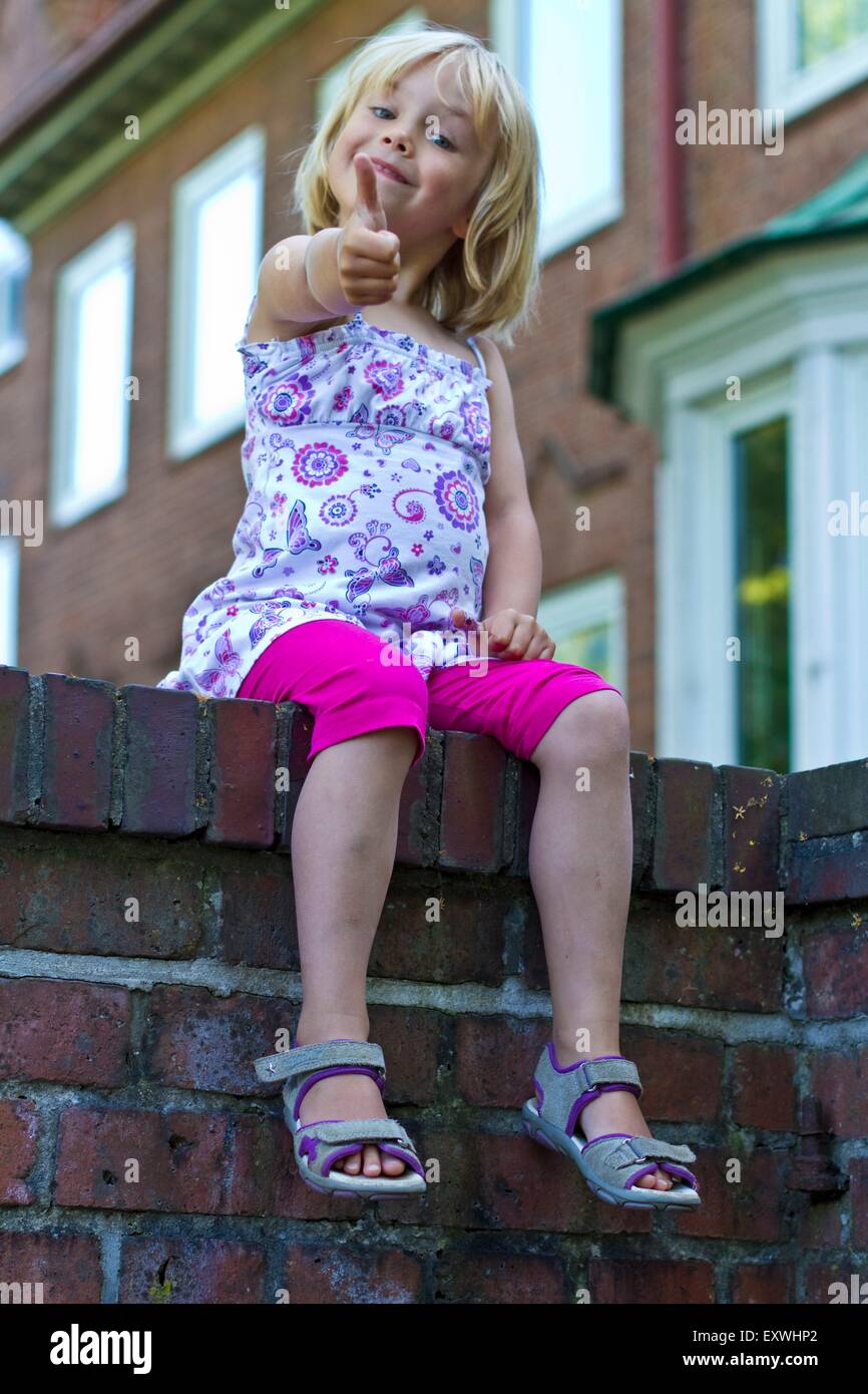 Girl sitting on a wall with thumps up Stock Photo
