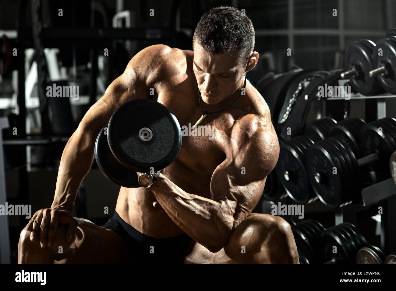 very power athletic guy bodybuilder ,  execute exercise with  dumbbells, in dark gym Stock Photo