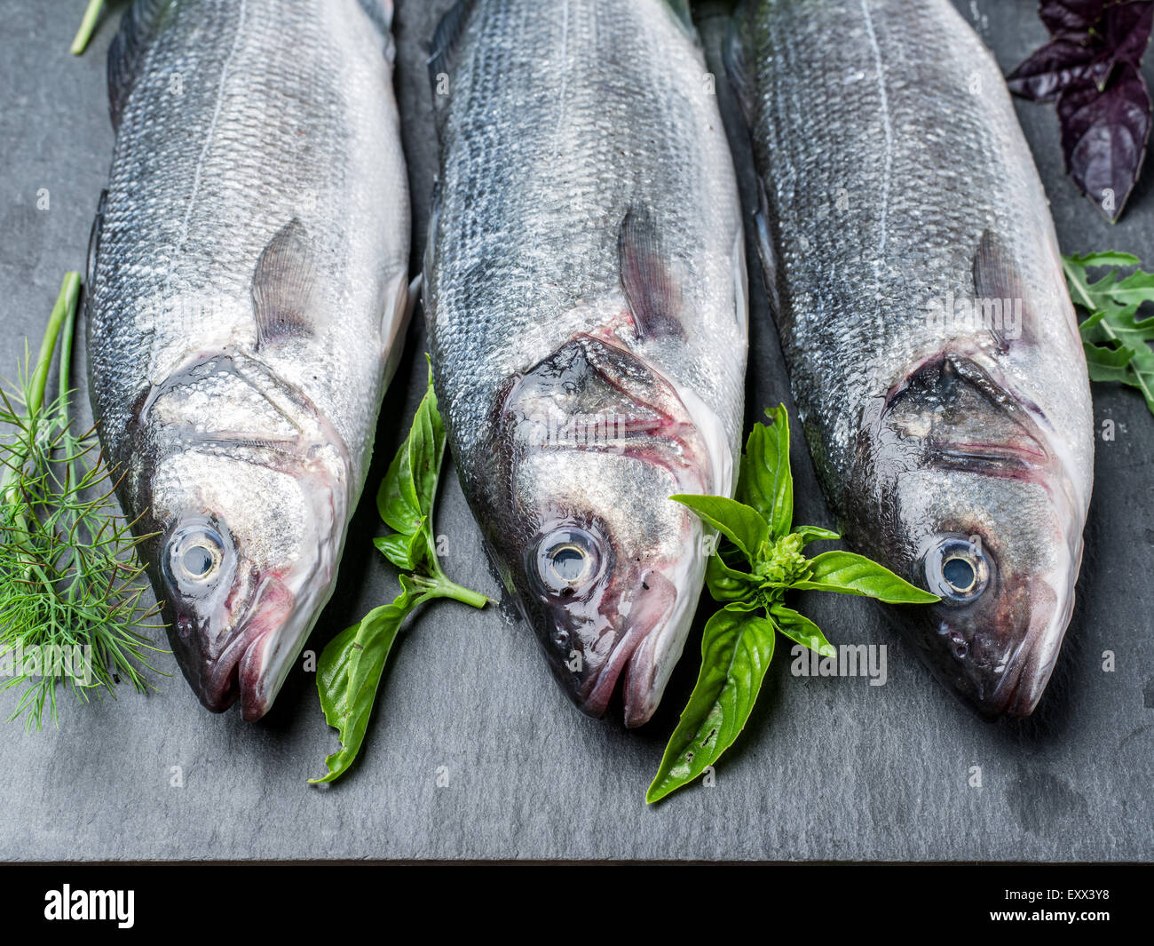Three fish - seabass on a graphite board with spices and herbs. Stock Photo