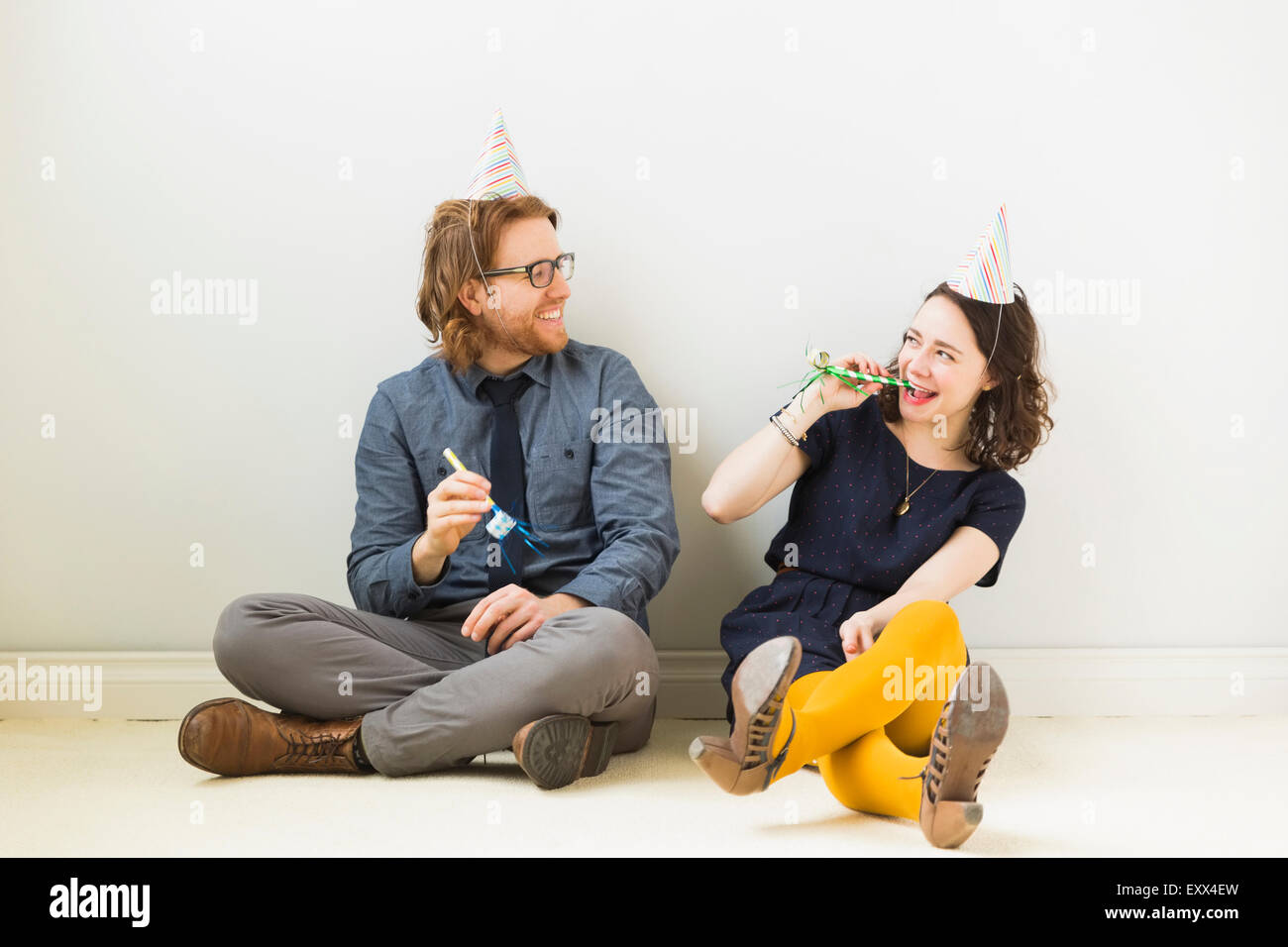 Couple with party horn blowers and party hats sitting on floor Stock ...