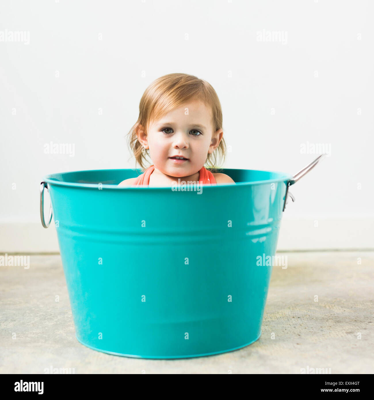 Little girl (2-3) sitting in turquoise bucket Stock Photo