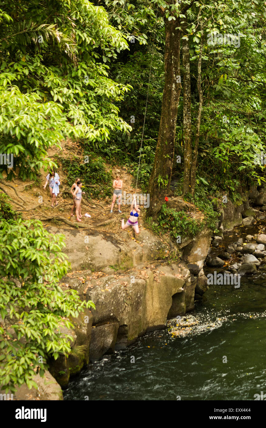 Women Swinging On Rope Swing Above River In Distance Stock