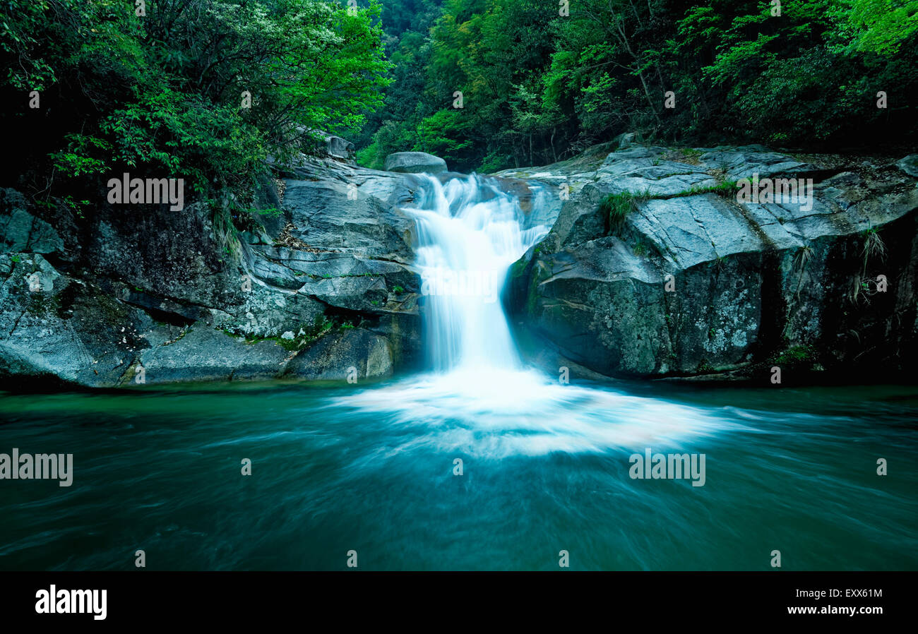 Large rain forest waterfall, sun beams, and mossy rocks Stock Photo
