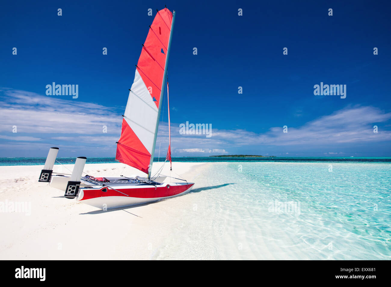Sailing boat with red sail on a beach of deserted tropical island with shallow blue water Stock Photo